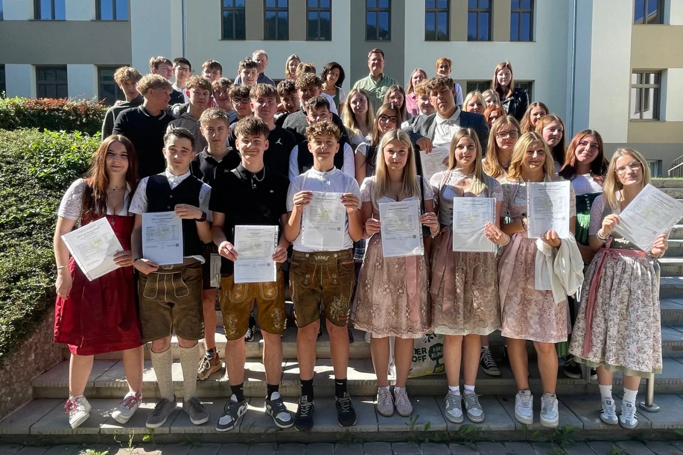 Schülerinnen und Schüler mit Zeugnissen vor Schulgebäude